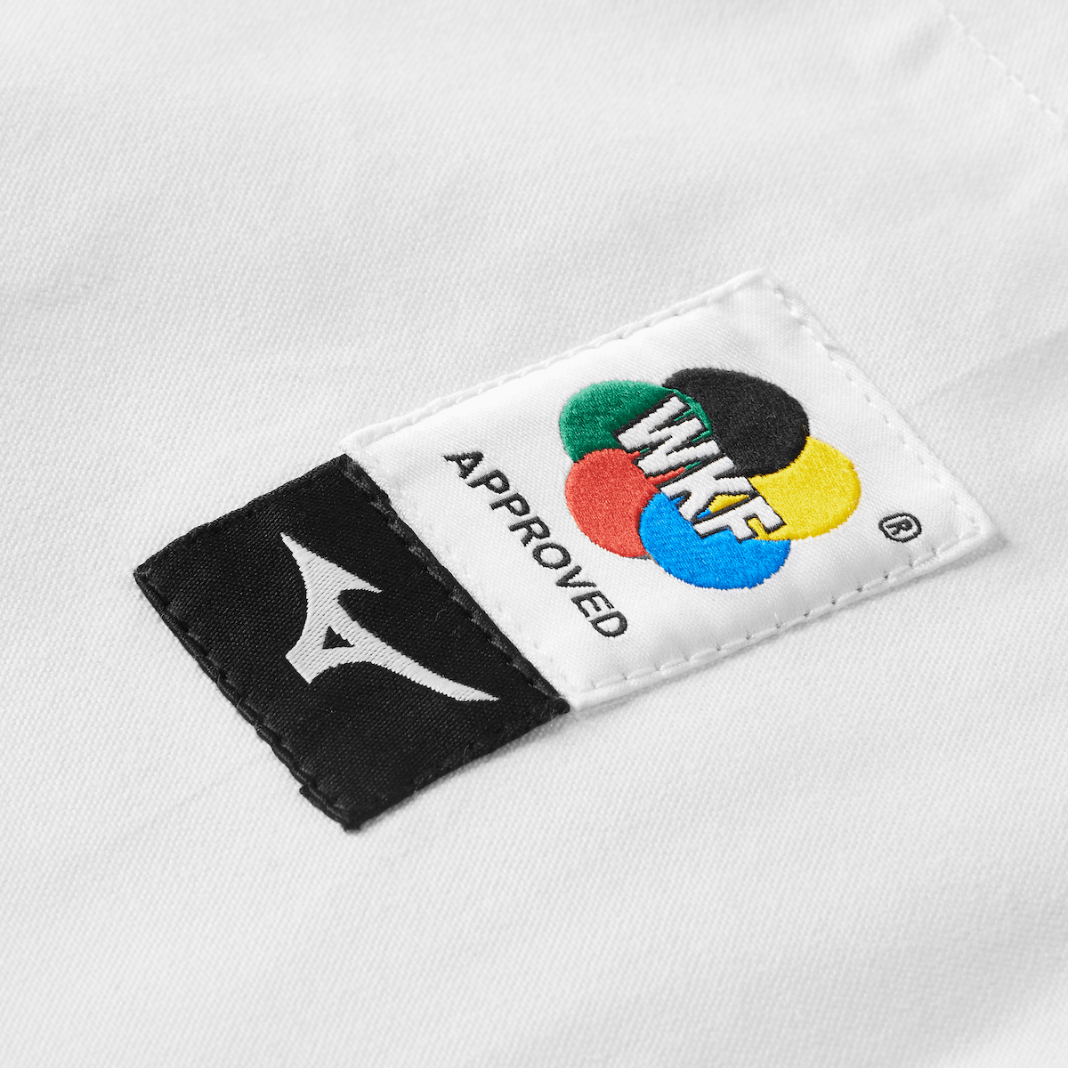 Close-up of WKF-approved Mizuno logo patch on white karate gi pants made of 12oz 100% cotton serge fabric