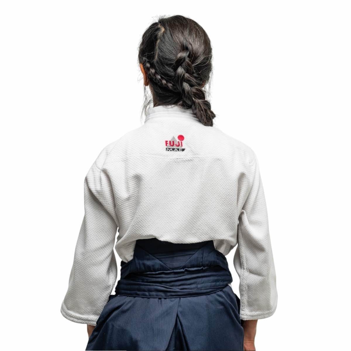 Back view of woman wearing white Fujimae Keikogi Aïkido gi jacket with navy hakama, designed for female training with reinforced shoulders and rice grain fabric texture