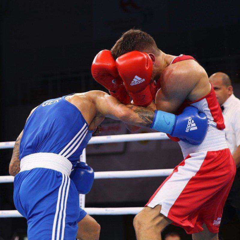 Deux boxeurs amateurs en compétition portant des gants de boxe Adidas homologués IBA, rouge et bleu.