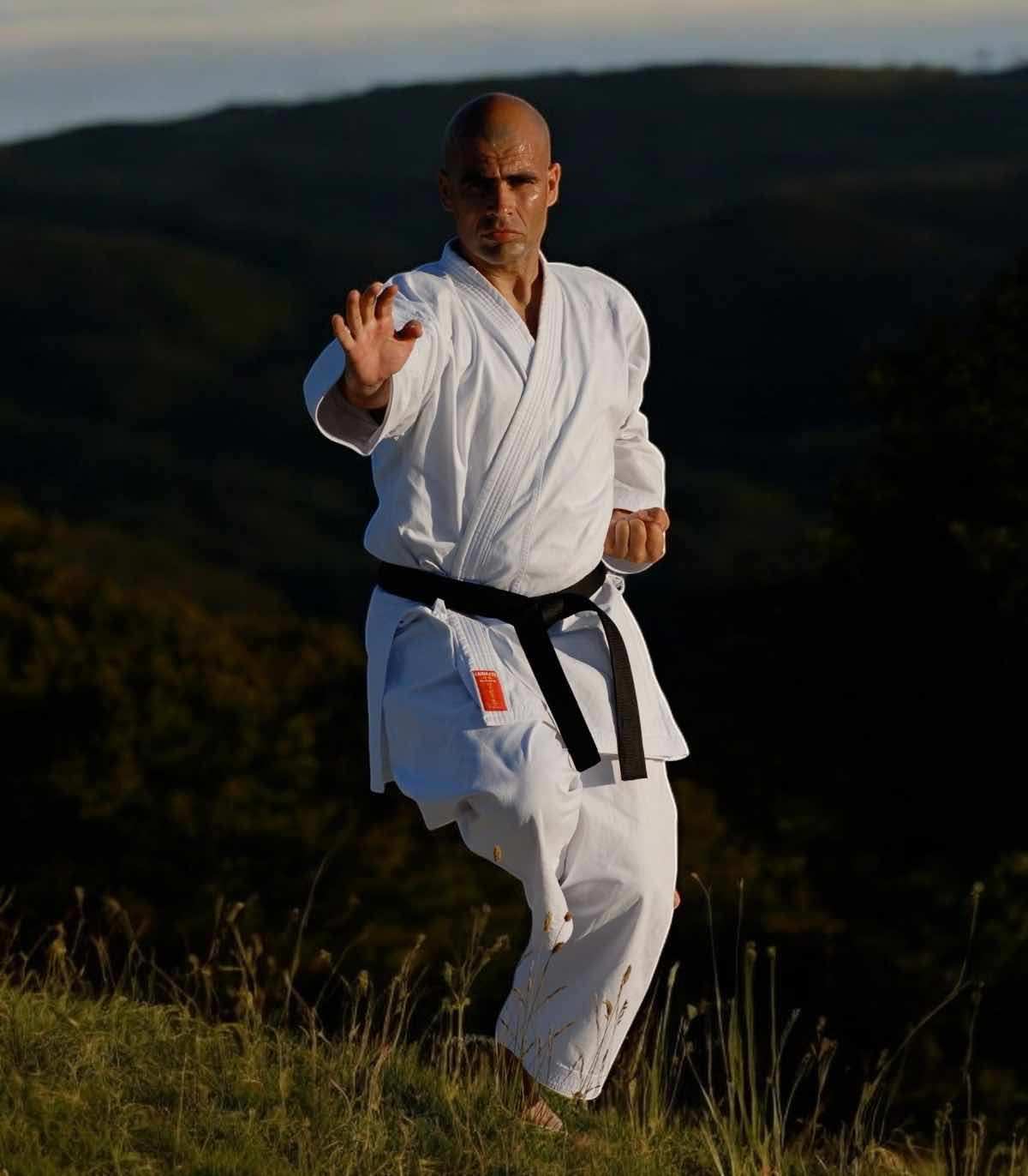 Man practicing karate wearing white Kimono Karate Kamikaze Europa with black belt outdoors