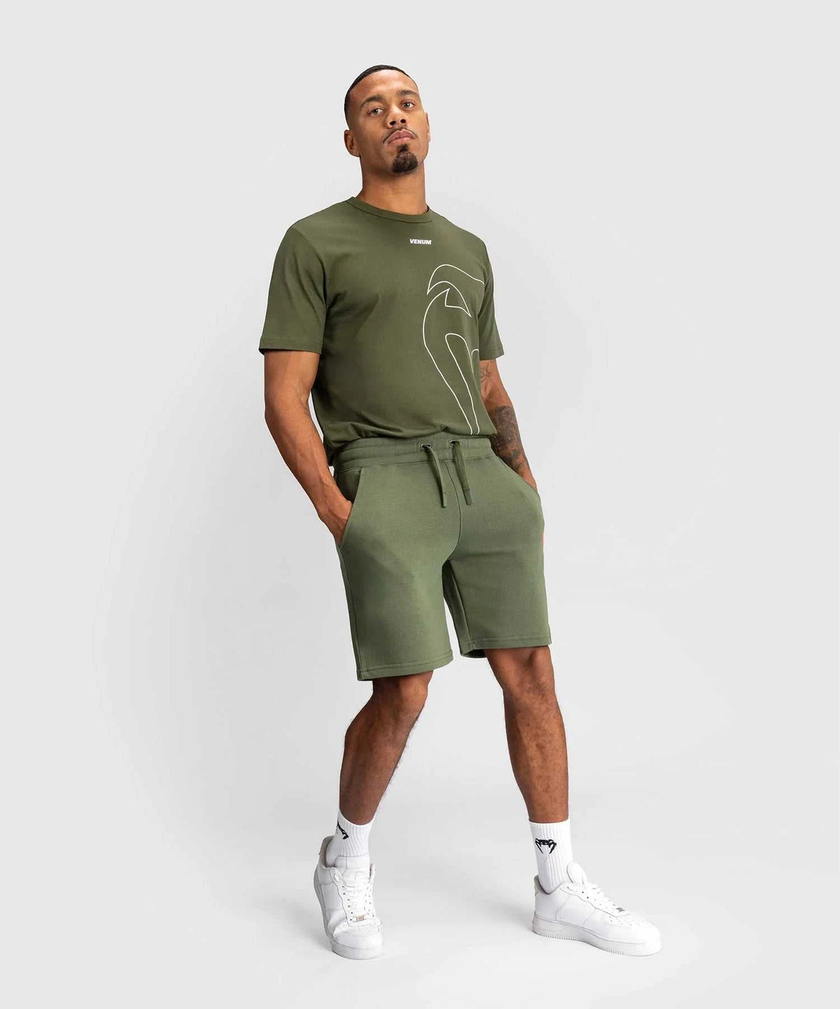 Man wearing kaki Shorts Venum Classic with elastic waistband and side pockets, paired with matching kaki t-shirt and white sneakers