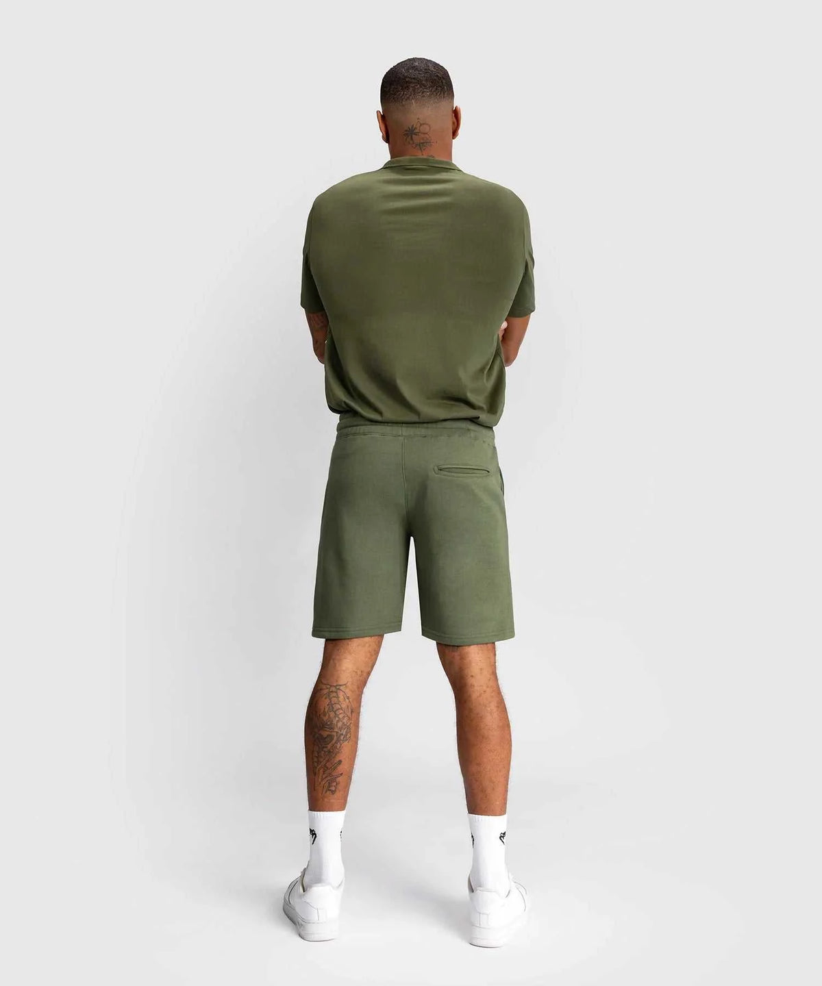 Back view of a man wearing kaki Shorts Venum Classic with matching t-shirt and white sneakers against a plain background