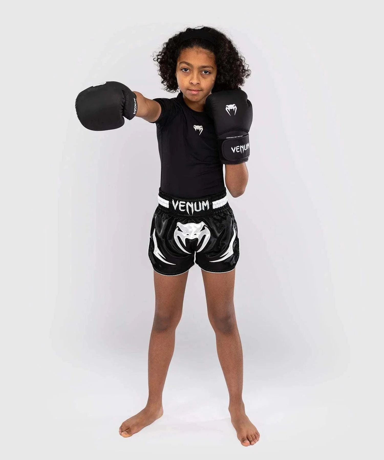 child wearing black Short Muay Thai Venum Inferno with boxing gloves in fighting stance