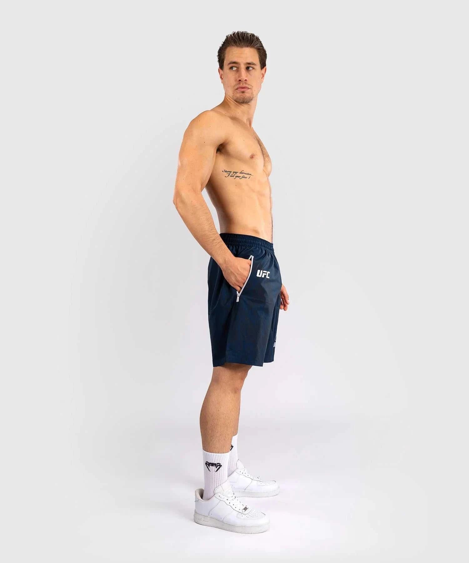 Man wearing navy UFC Fusion par Venum performance shorts with zippered pockets and elastic waistband.