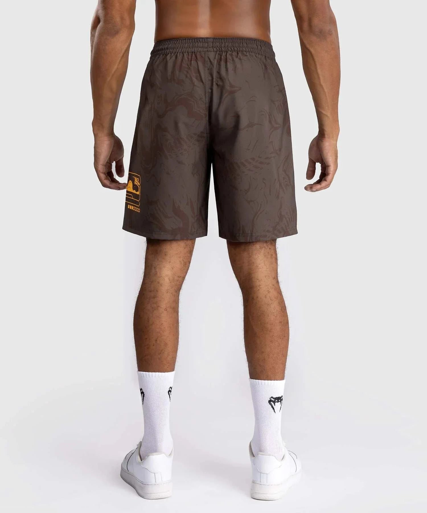 Back view of man wearing brown UFC Fusion par Venum performance shorts with elastic waistband and zippered side pockets.