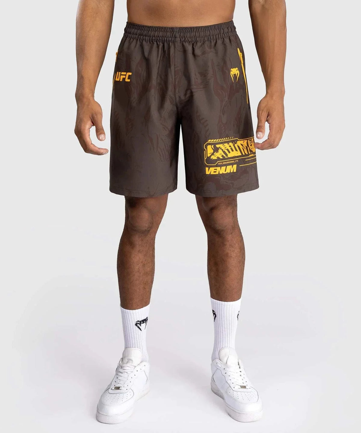 Men wearing brown UFC Fusion par Venum performance shorts with yellow logos and white sneakers.