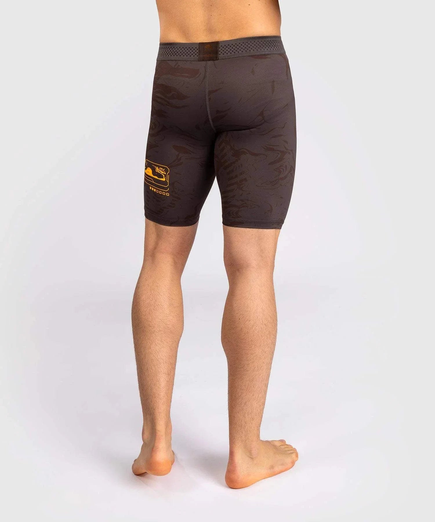 Back view of man wearing black and brown UFC Fusion par Venum compression shorts with elastic waistband and nature-inspired design.