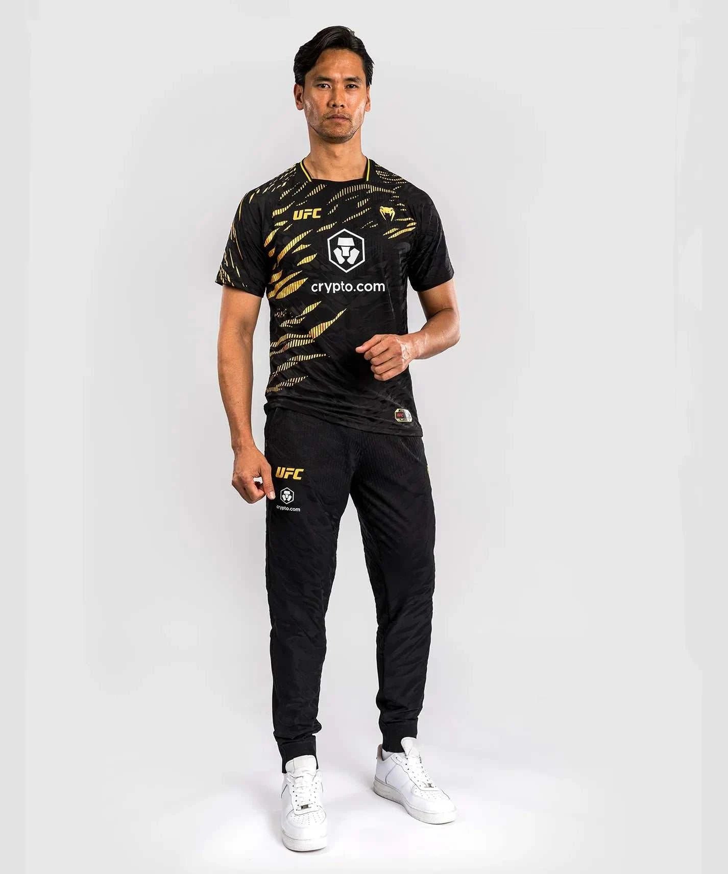 Male model wearing black and gold UFC Fusion par Venum Dry-Tech performance T-shirt with short sleeves and printed logos.