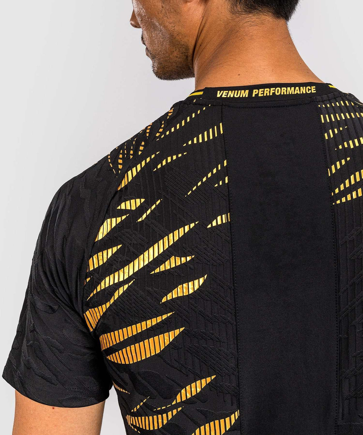 Back view of a man wearing a black and gold UFC Fusion par Venum Dry-Tech performance T-shirt with short sleeves and ventilated collar.