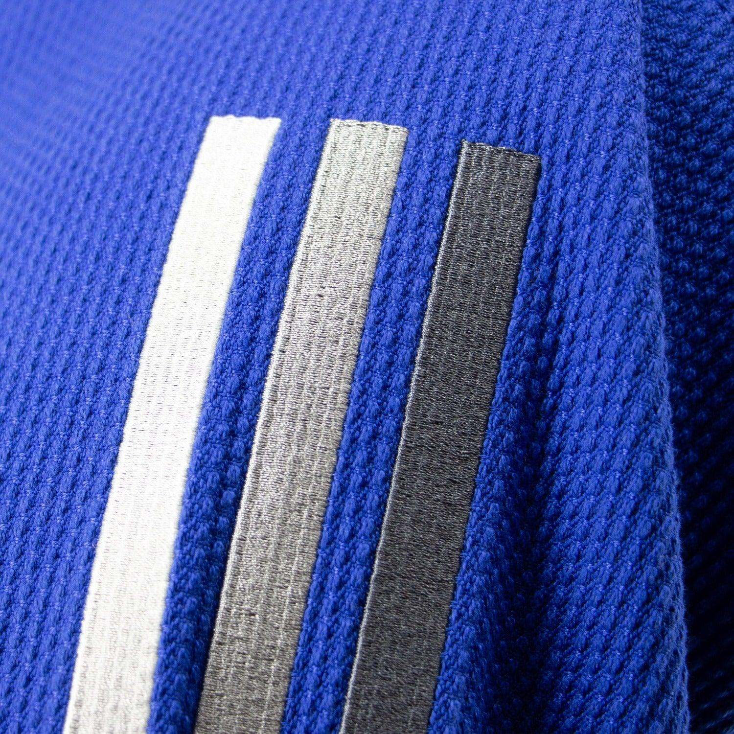 Détail textile bleu du kimono de JJB Adidas Contest 2.0 avec bandes grises dégradées.