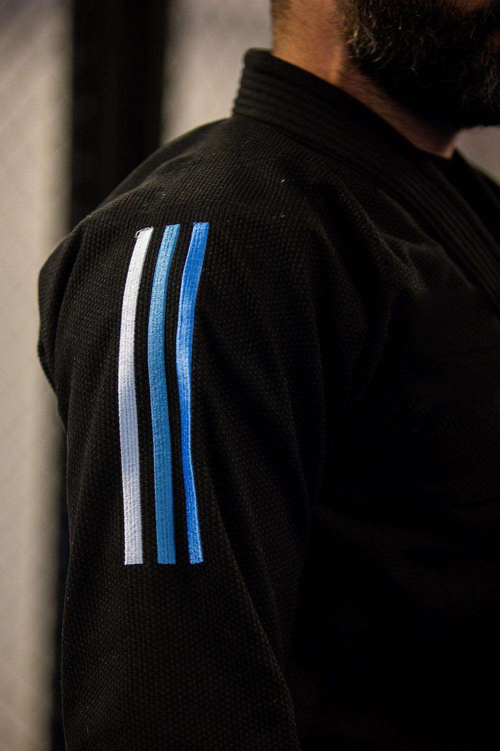 Kimono de JJB Adidas Contest 2.0 noir avec bandes bleues dégradées, veste en Pearl Wave polycoton et pantalon ripstop renforcé.