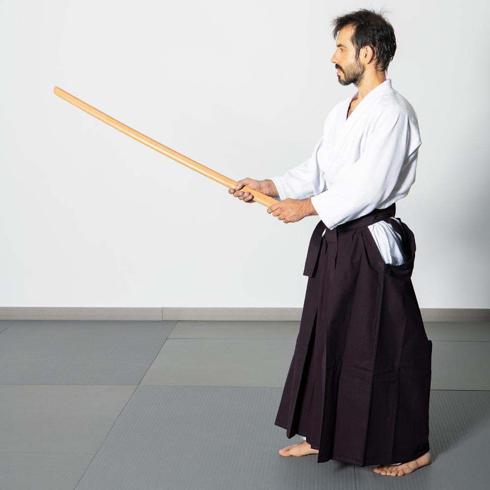 Homme en tenue d'aïkido tenant un bokken hêtre Fuji Mae en bois naturel.